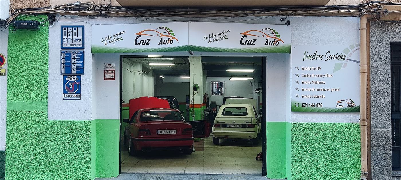 Puerta abierta del taller con dos coches dentro y el cartel de servicios