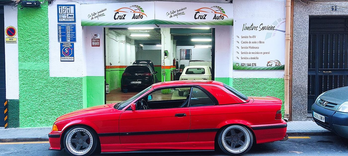 Fachada verde y blanca de CRUZAUTO con un BMW rojo aparcado delante